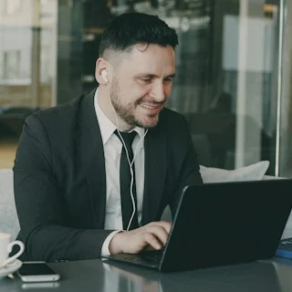 A man in a suit smiling at his laptop.