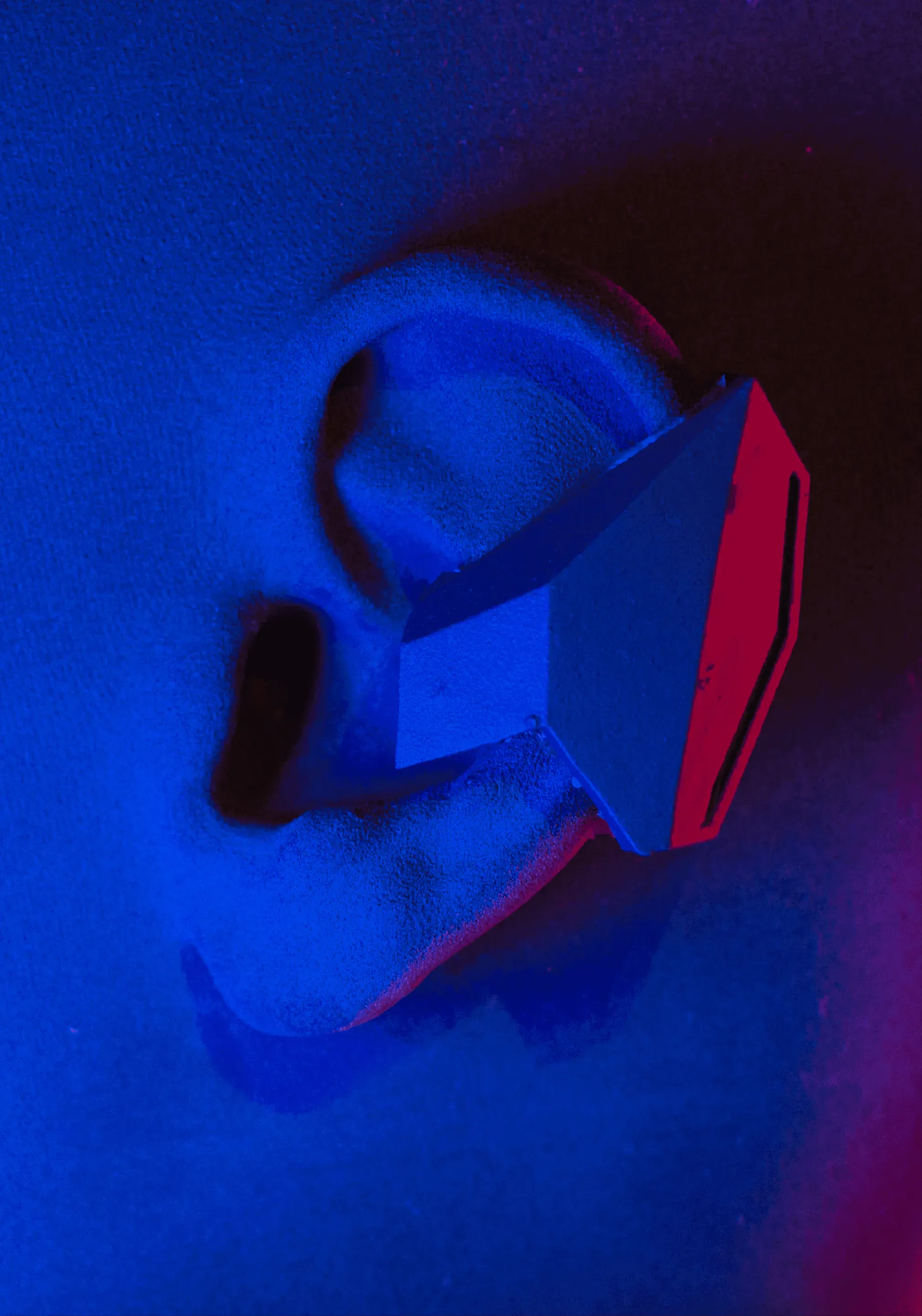 The earbud prototype clipped onto a model of an ear, photographed close in deep blue light. One facet of the earbud is lit red.