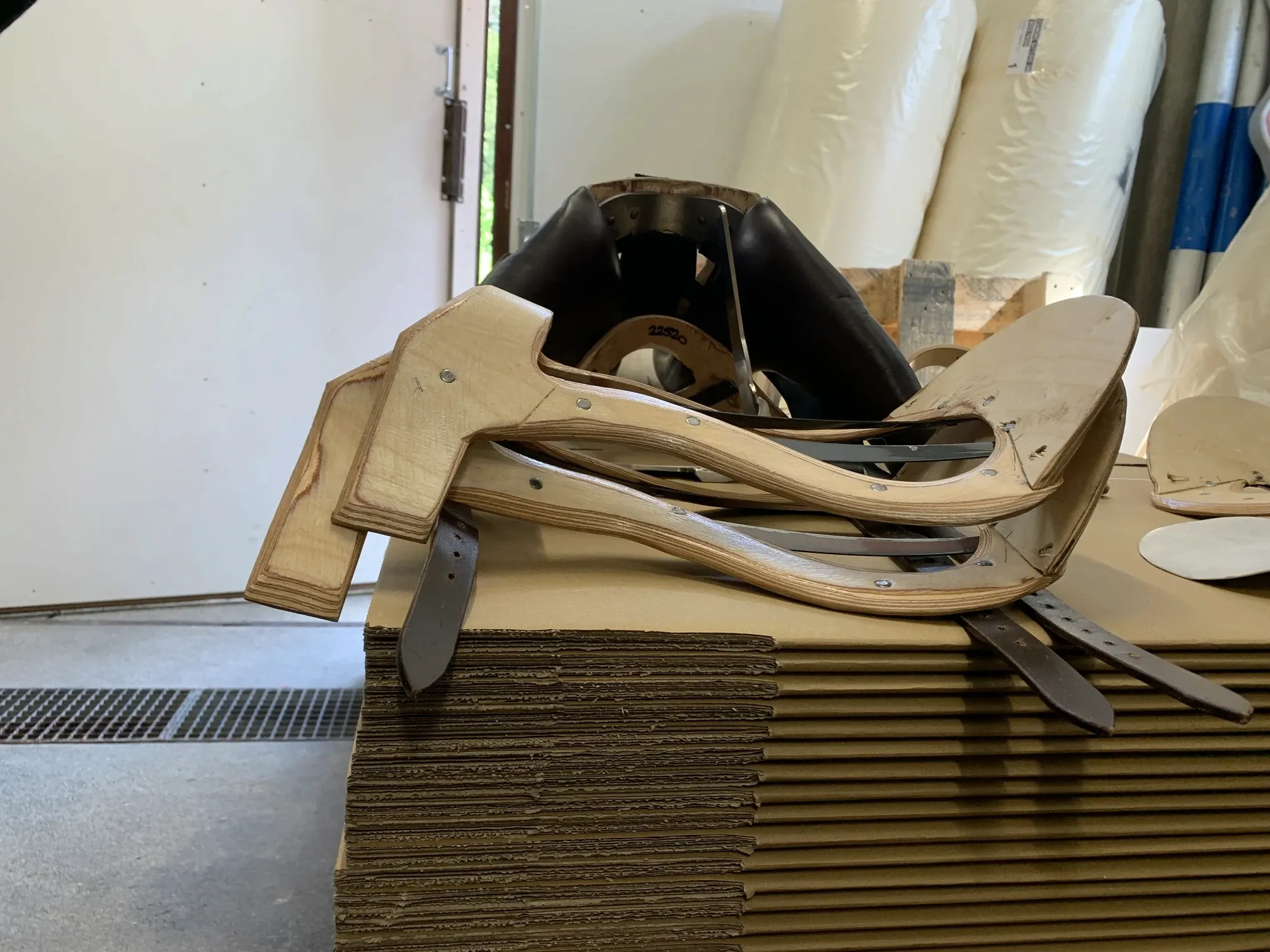 Bare wooden saddle trees with metal fittings stacked on sheets of cardboard in a workshop.