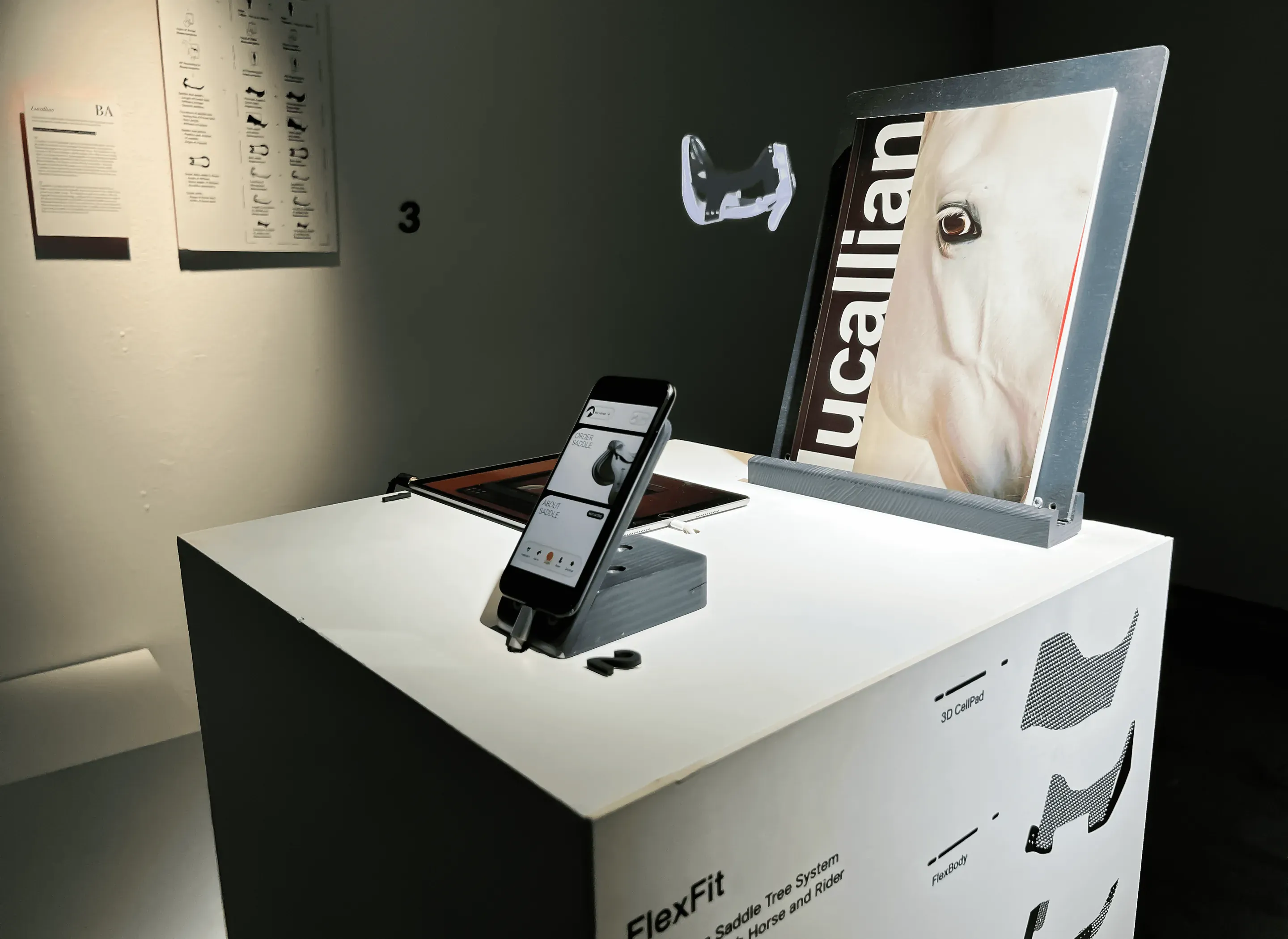 A white plinth with a phone on a stand and a board with the Lucallian wordmark over a close up of a white horse's eye. The plinth is printed with the word FlexFit and outlines of the parts.
