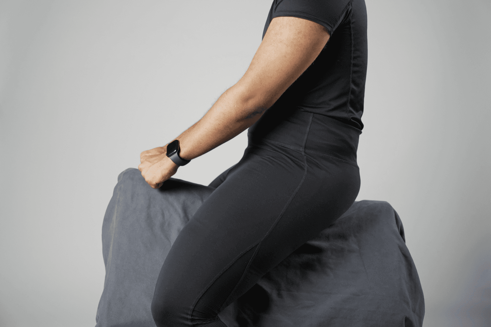Seat study: side view of a person wearing a watch, sitting astride the block and gripping its front edge.