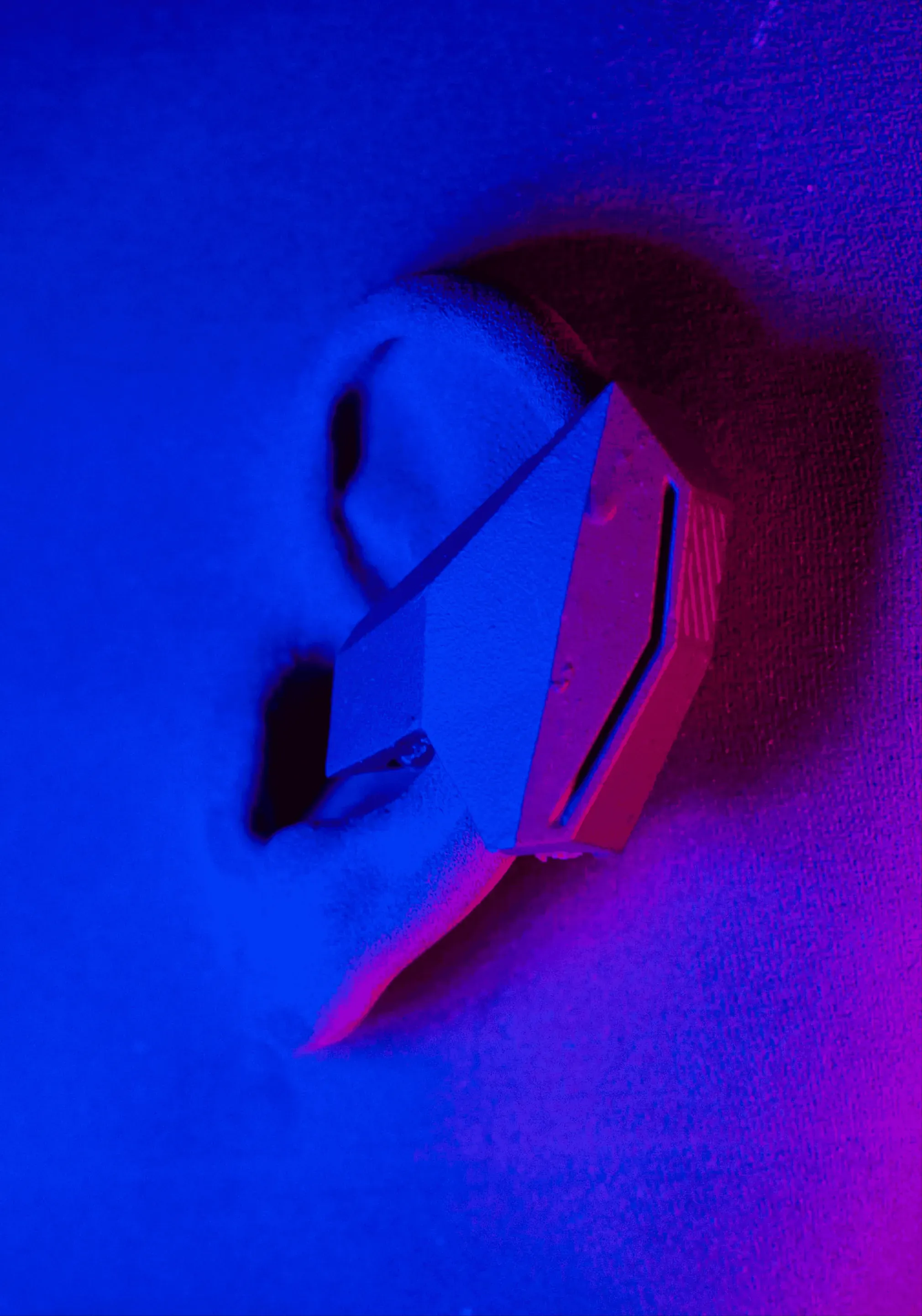 The earbud prototype on a model of an ear, seen from the side in blue and magenta light.
