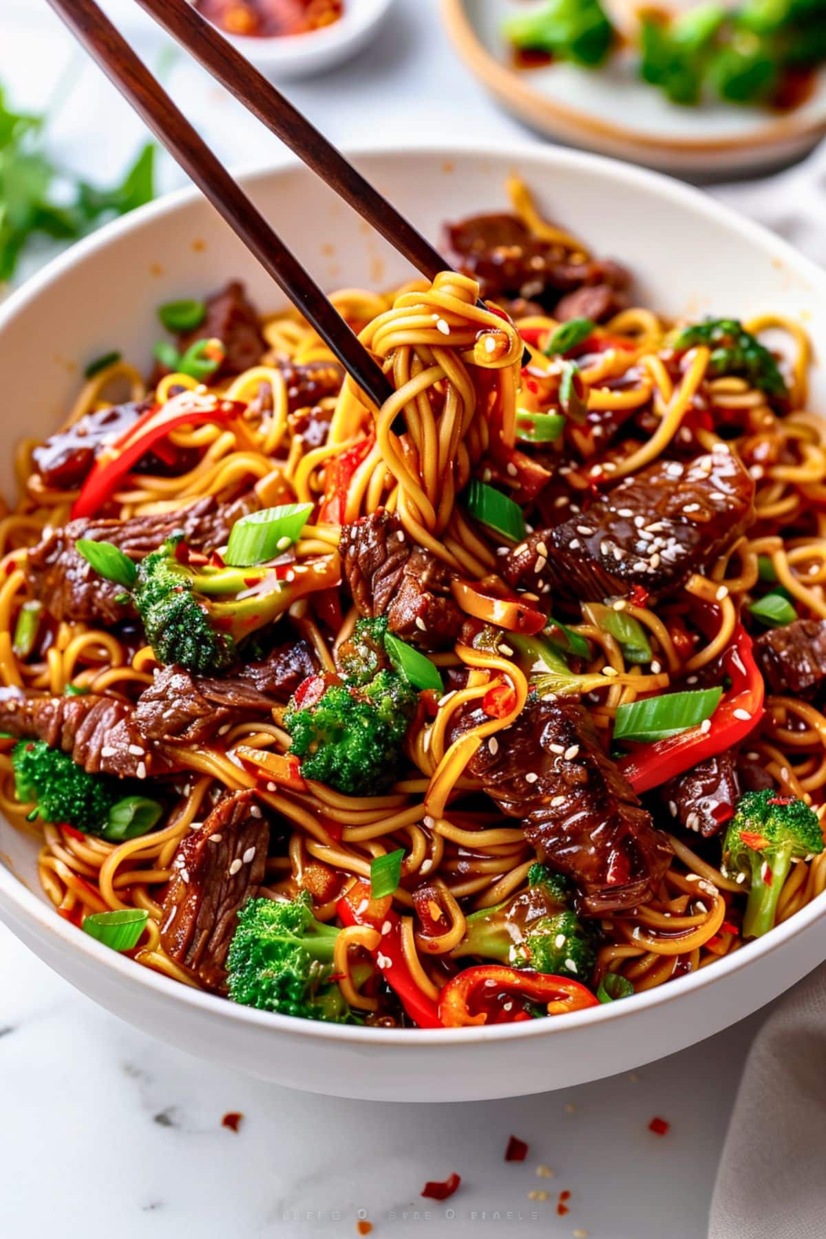 Moodboard reference: a white bowl of noodles with beef, broccoli and red pepper, seen from above, with chopsticks lifting some noodles.