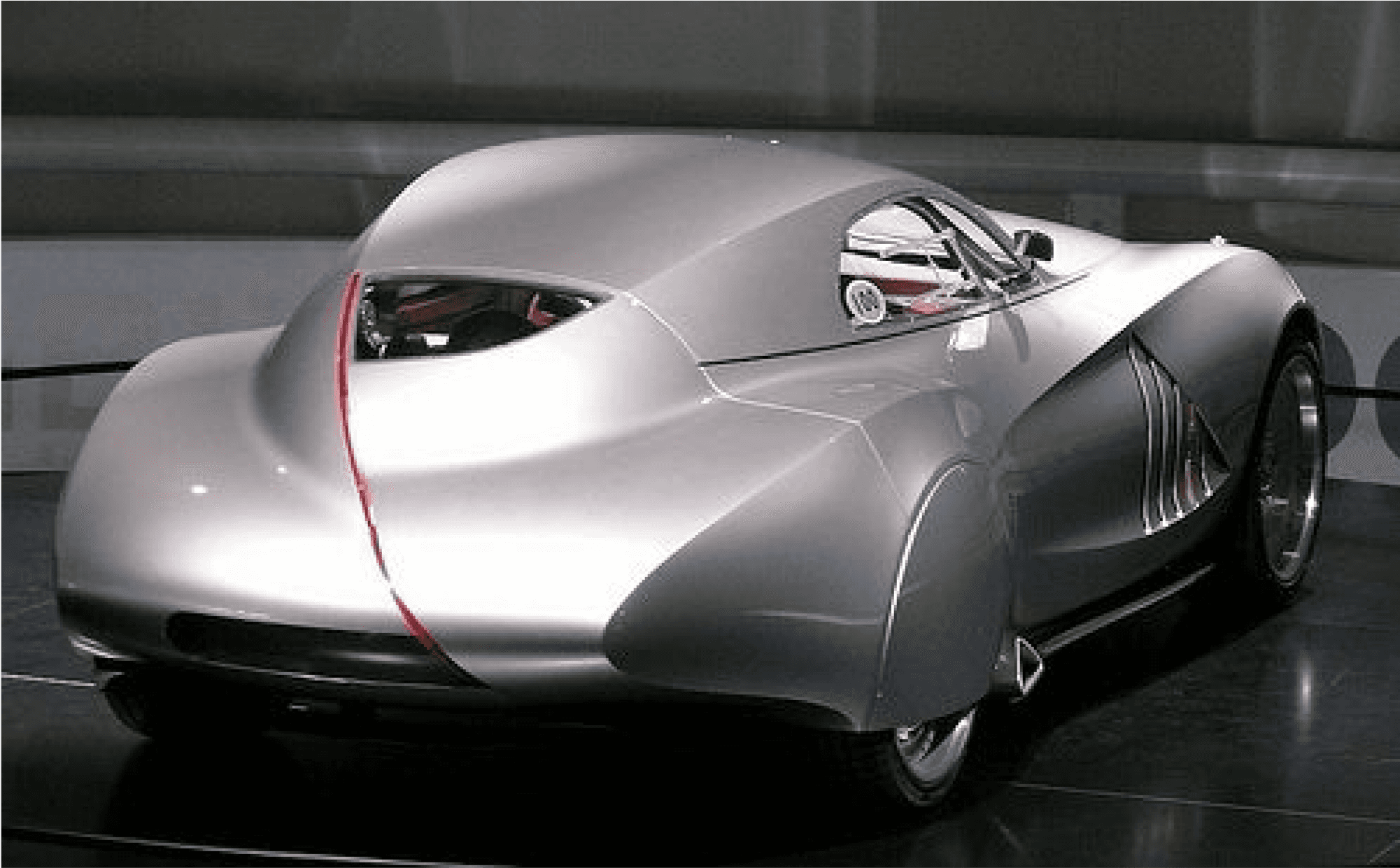 Moodboard reference: a silver streamlined concept car with a red seam, in a dark showroom.