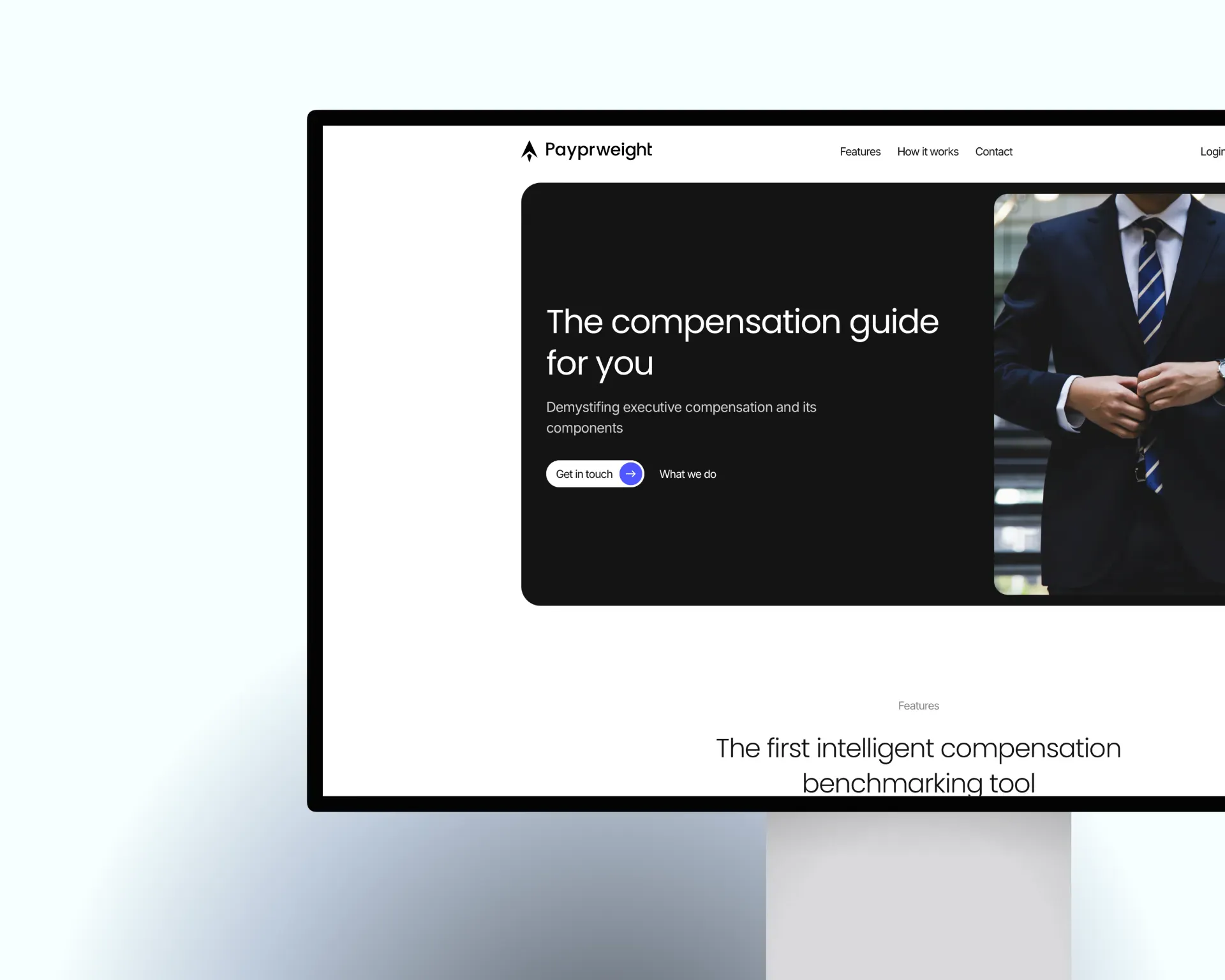 A black framed monitor on a pale blue ground, cropped at the right edge, showing the Payprweight website: the logo and a navigation with Features, How it works and Contact, a black rounded panel with the line The compensation guide for you and the buttons Get in touch and What we do, a photo of a person in a dark suit and striped tie, and below it the heading The first intelligent compensation benchmarking tool.