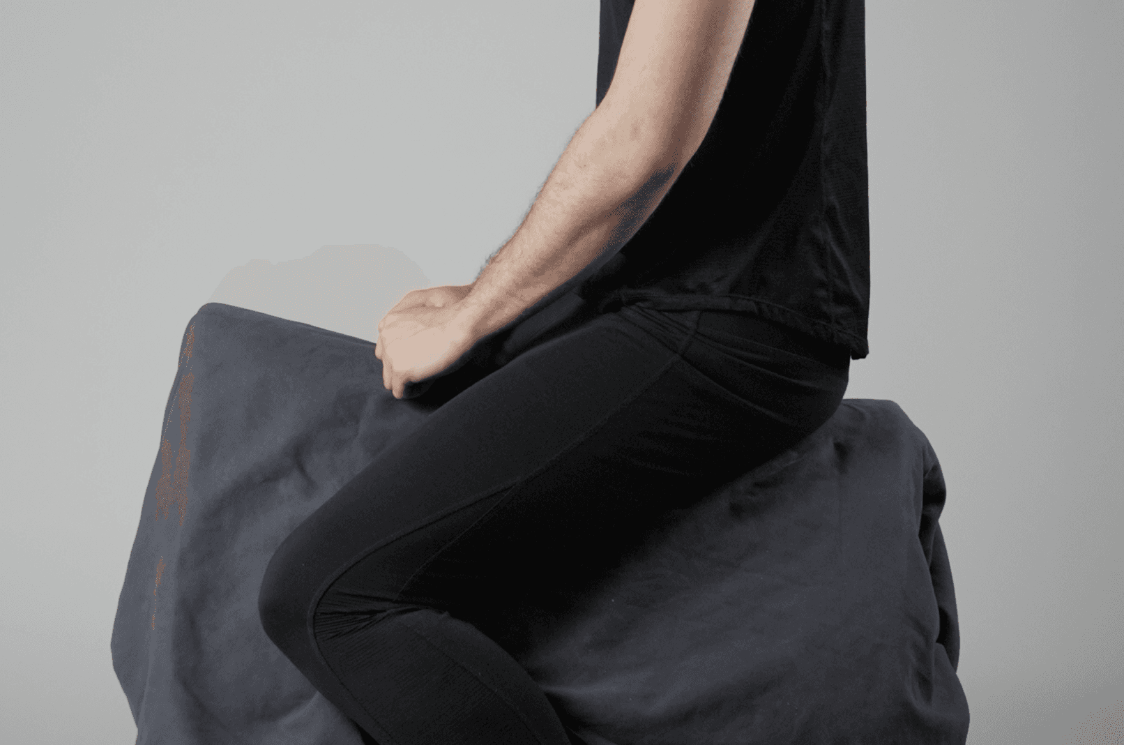 Seat study: side view of a person sitting astride the block, hand on the front edge, legs hanging down.