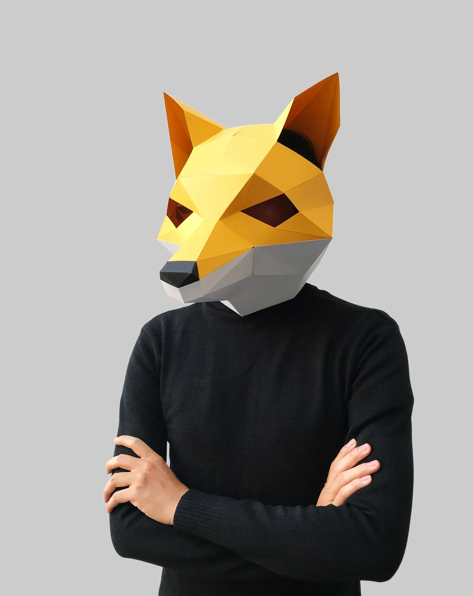 Moodboard picture: a person in a black jumper with crossed arms wears a yellow low poly fox mask made of flat faces.